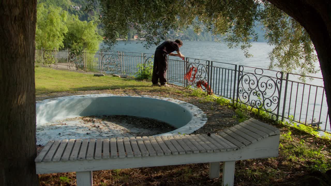 Solitary man in garden with empty pool overlooking Lake Como, Italy (Lago di Como, Italia) at golden hour, contemplative mood