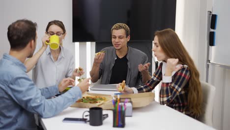 Freundliche,-Fröhliche,-Vielfältige-Teamarbeiter-Reden-Lachend-Und-Essen-Gemeinsam-Pizza-Im-Büro