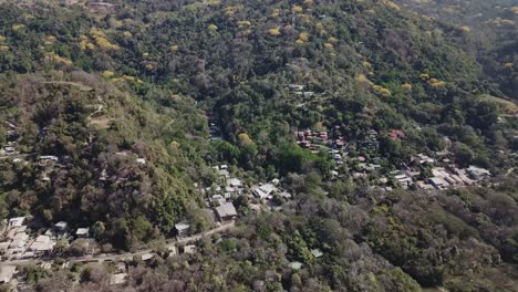 Drone-footage-flying-towards-the-surf-beach-town-of-Santa-Teresa,-Costa-Rica,-surrounded-by-tropical-forest-and-green-mountains-in-the-background