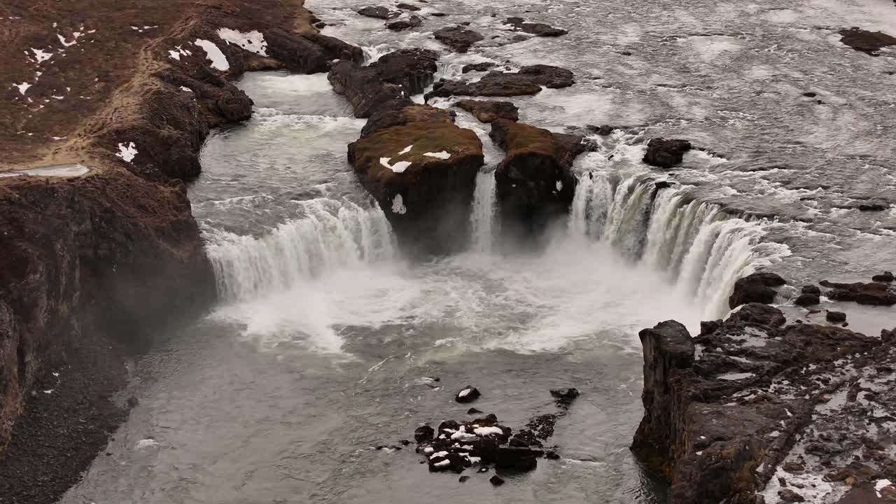 Majestic aerial shot of Goðafoss waterfall thundering over basalt cliffs in northern Iceland, with icy water carving through Skjálfandafljót River near Laugar.