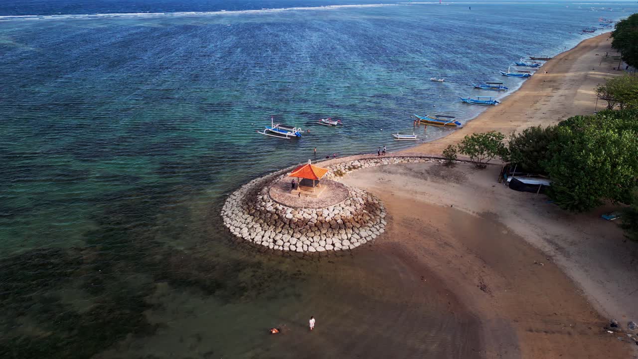 Aerial drone view of Sanur Beach Bali with turquoise waters, sandy coast, protective wave barriers, and a small fishing boats creating a mix of culture and natural beauty
