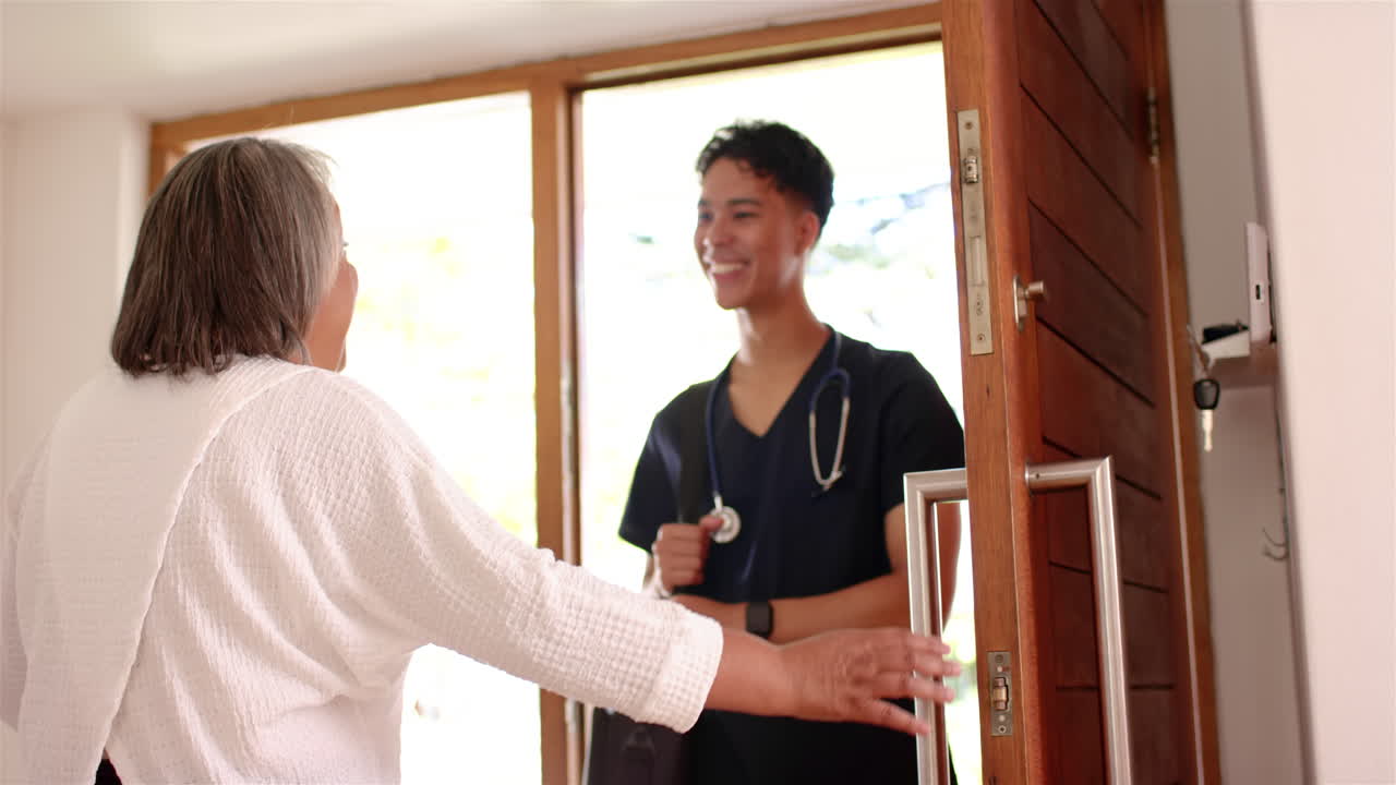 Smiling male physiotherapist with stethoscope greeting senior female at home door