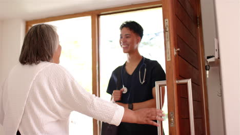 smiling male physiotherapist with stethoscope greeting senior female at home door