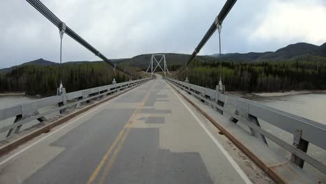 punto de vista a través de la ventana trasera mientras conduce la autopista de alaska sobre el puente colgante sobre el río liard en el parque provincial de aguas termales de liard en las montañas rocosas del norte de canadá en columbia británica