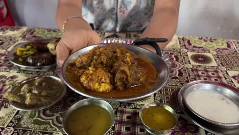a close-in shot of a woman holding a steel plate, showcasing the rich and flavorful mutton curry.