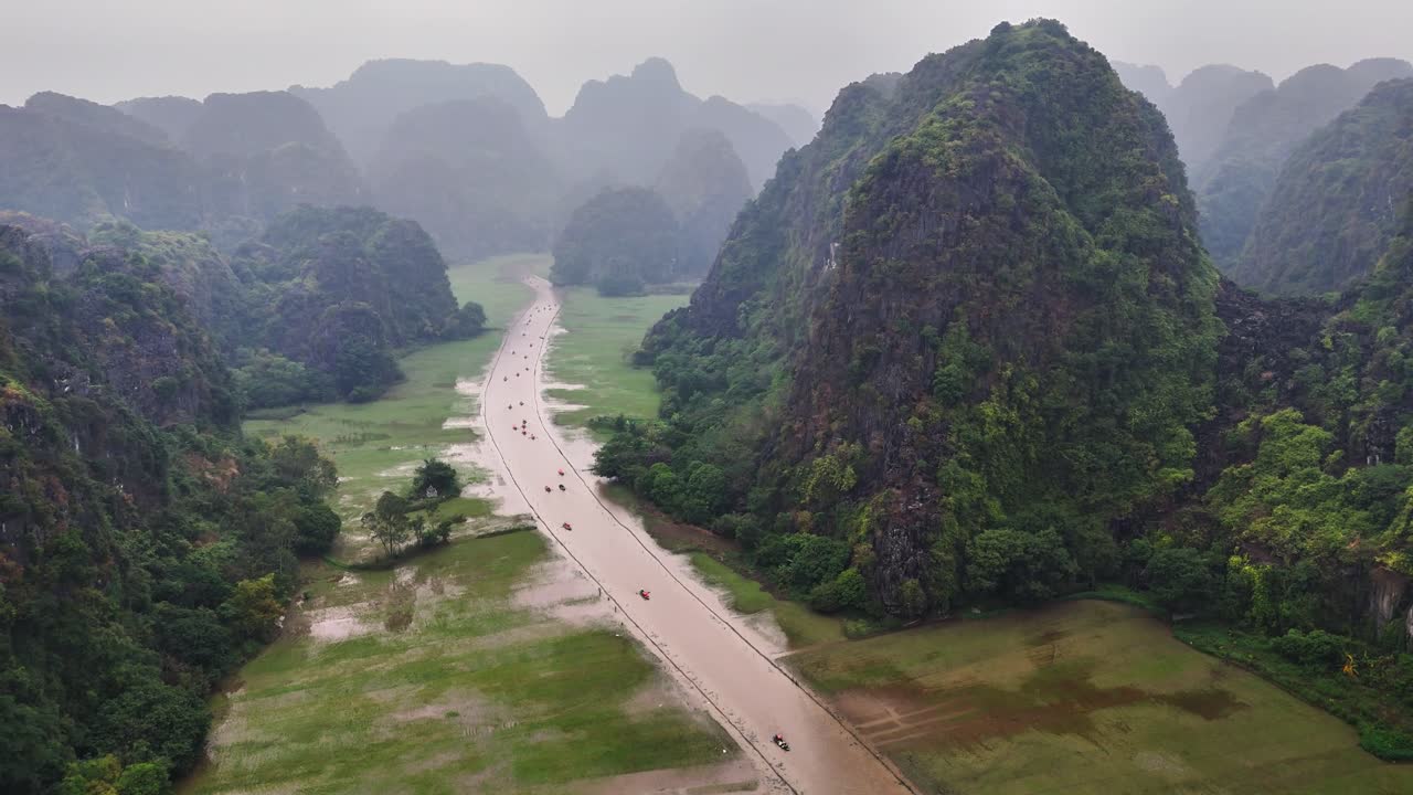 A winding river flows through lush green rice fields and dramatic limestone karsts in Hang Mua, Tam Coc, Ninh Binh, Vietnam, surrounded by misty mountains in a serene and natural setting