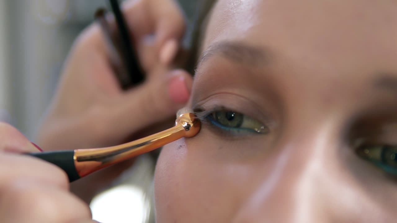 Eyes make up process. Artist corrects eye line using a professional brush with golden edge. Close up of a model's face