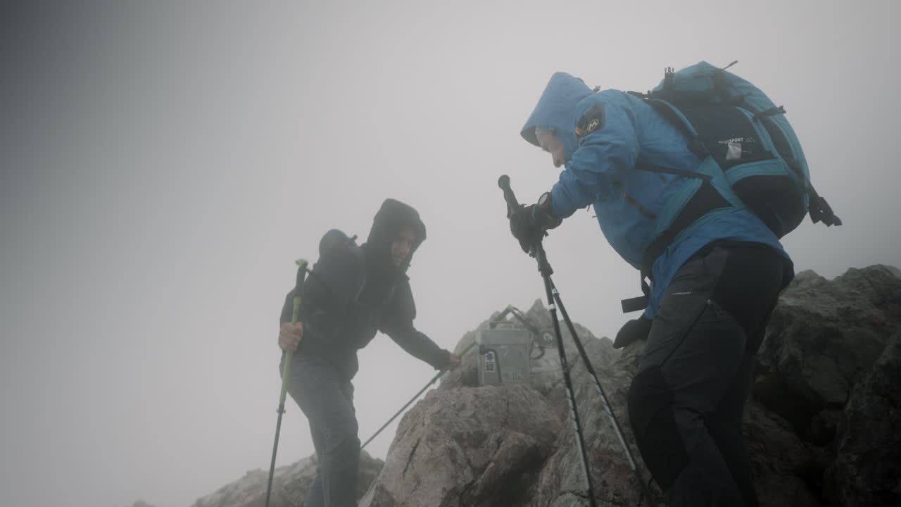 dos excursionistas que llegan a la cima del stol de la montaña, descansando en condiciones de viento y nubosidad baja