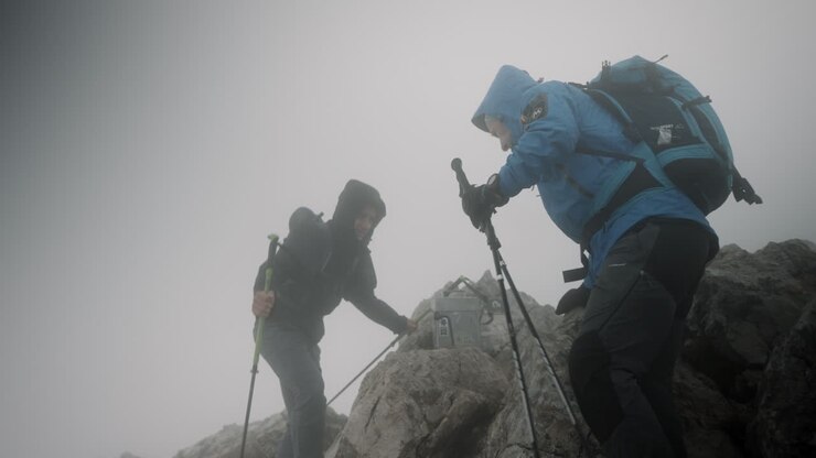 Two hikers reaching top of the mountain Stol, taking a rest in windy conditions and low cloud cover