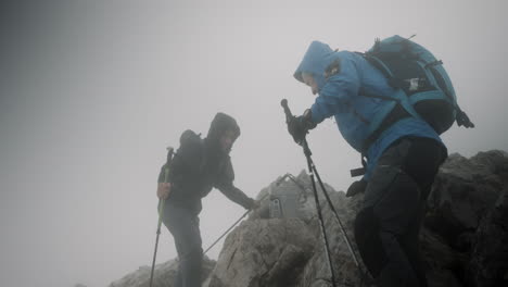 two hikers reaching top of the mountain stol, taking a rest in windy conditions and low cloud cover