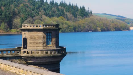 Lady-Bower-Staudammturm-Im-Lady-Bower-Stausee-Mit-Blick-Auf-Den-Stausee-Und-Den-Wald-In-Der-Ferne-Vom-Peak-District,-Sonniger-Tag,-Ruhige-Wellenaufnahme-In-4K