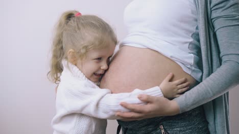 una niña pequeña abraza a su madre embarazada en un fondo blanco en la habitación