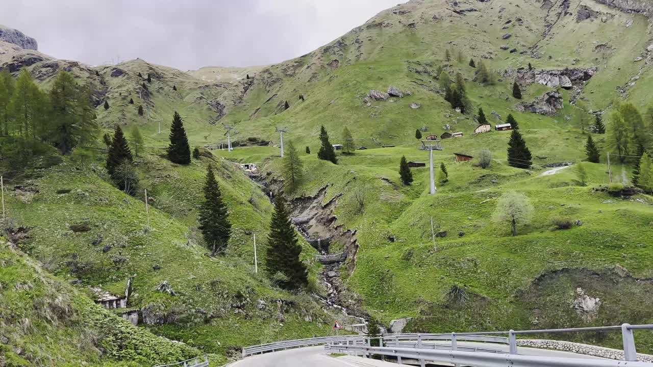 Lush green meadows, pine trees, and a mountain stream shape the dramatic curves of Giau Pass in the Dolomites — one of Italy’s most scenic alpine routes