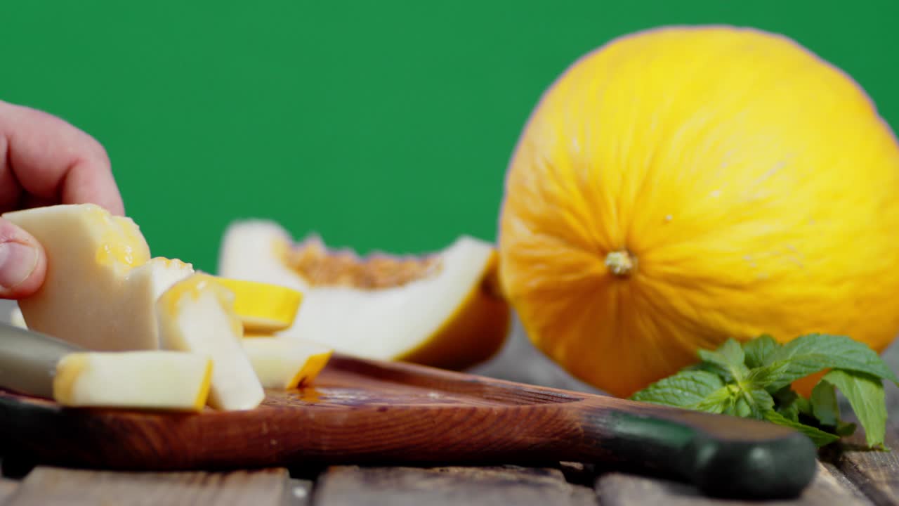 Male hand with a knife cut the melon into small pieces.