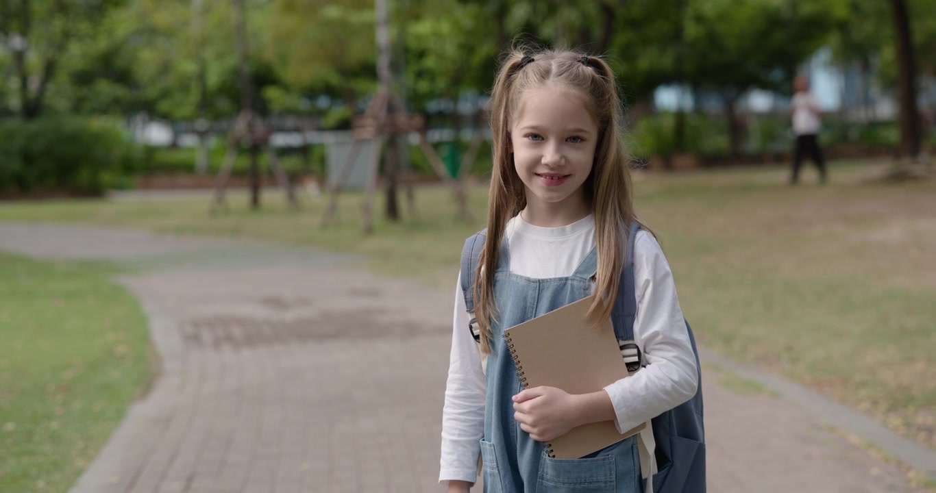 Blij jong schoolmeisje met rugzak en notitieboekje lachend in een park