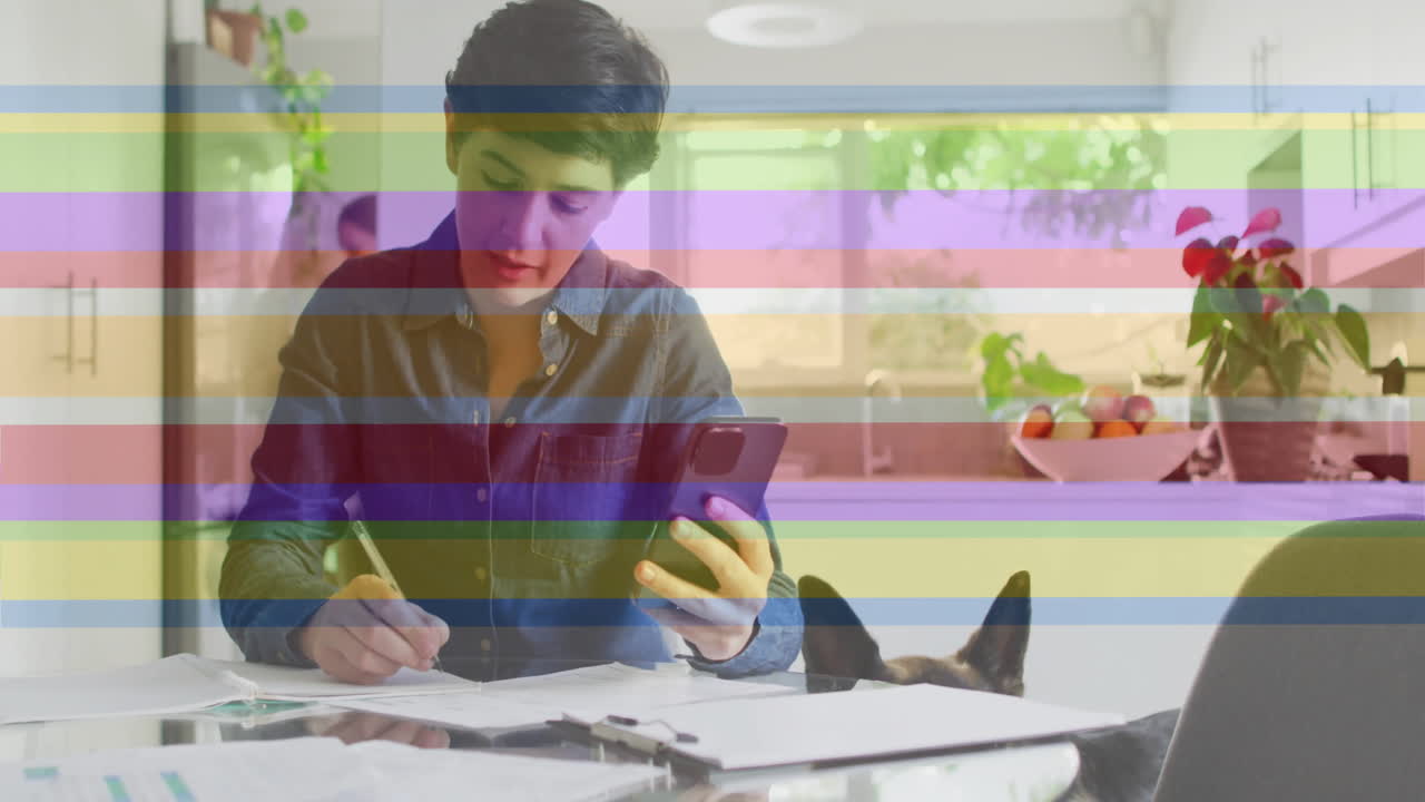 animación de orgullo rayas de arco iris sobre caucásico usando teléfono inteligente trabajando en la cocina con perro mascota