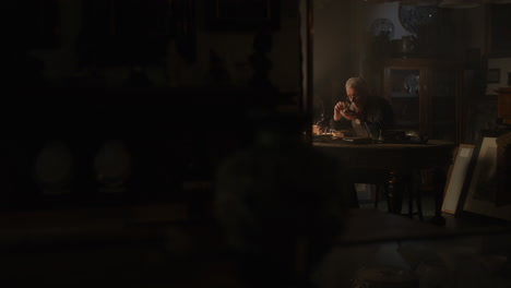 older passionate man evaluates an old silver skull watch in his office at night