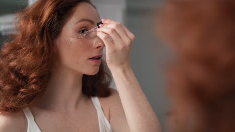 mujer caucásica usando suero para la cara en el baño.