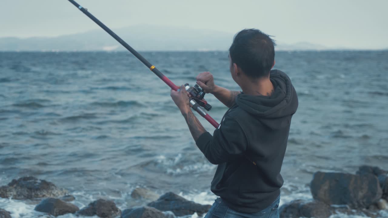 바람 부는 해변 해안선에서 낚싯대를 잡고 고군분투하는 청년