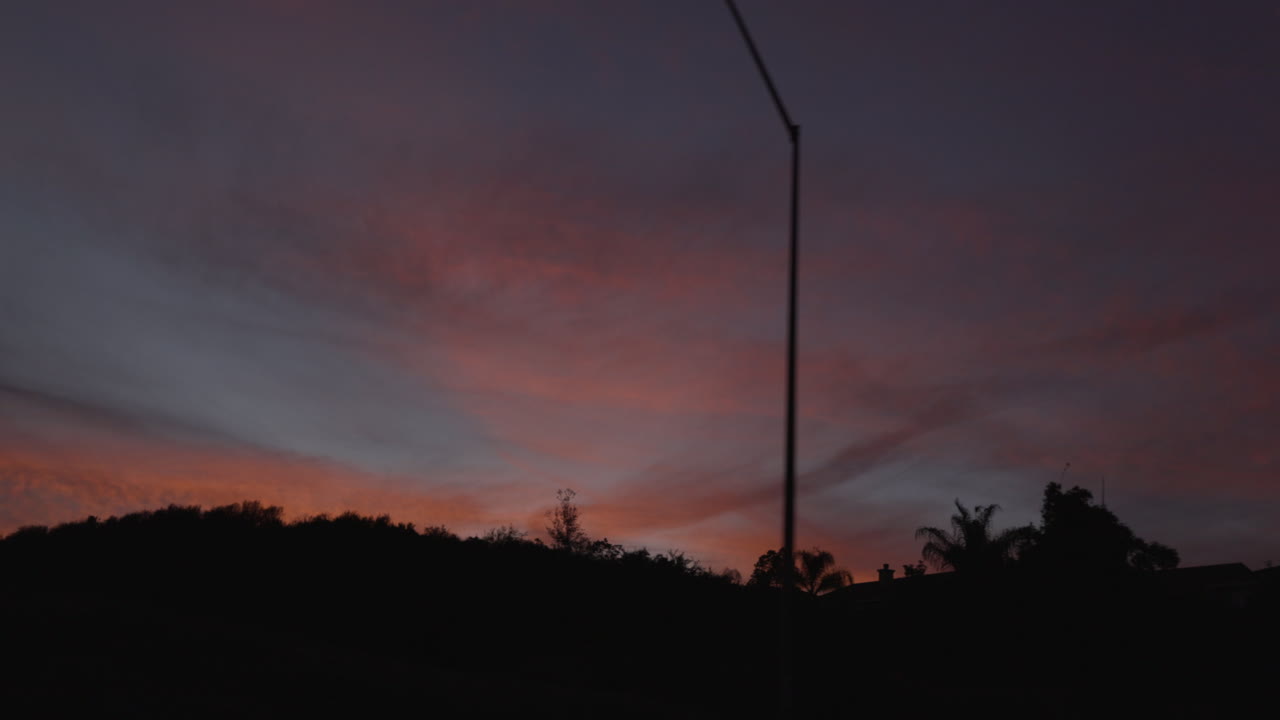 Cinematic slow-motion passenger POV on a Southern California highway as palm trees and suburban houses pass in silhouette against a glowing orange and pink sunset sky