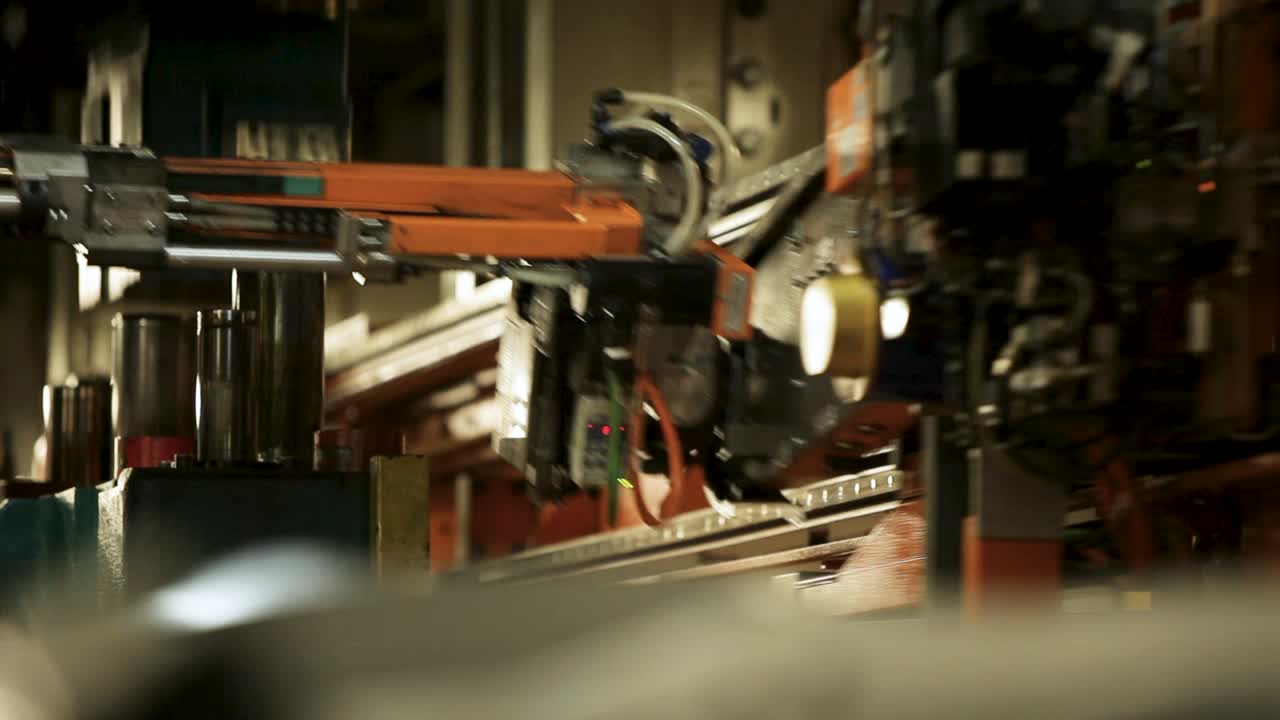 A large orange metal frame bearing a black camera and various equipment rides on a track through a warehouse, as captured by a handheld camera, with a blurred metal railing in the foreground