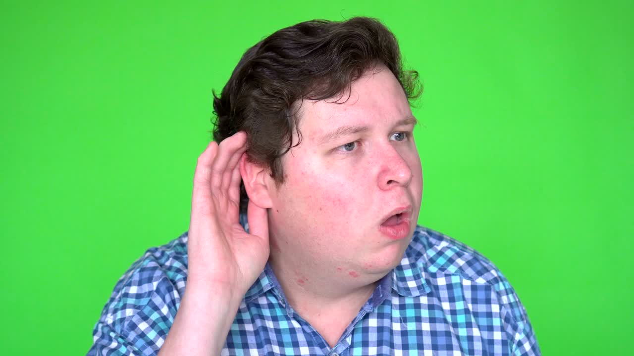 Young man eavesdropping and making funny facial expression on green screen