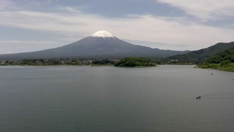 Aerial-of-iconic-and-majestic-volcano-Mount-Fuji-with-scenic-landscape,-lake-Kawaguchi,-boat,-and-snow-capped-peak-in-Fuji,-Japan