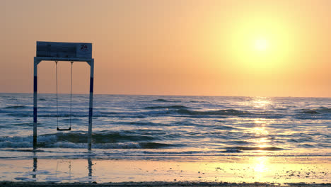 lonely swing stands by the ocean at sunset, waves gently rolling onto the shore