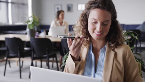 Happy-caucasian-casual-businesswoman-talking-on-smartphone-and-using-laptop-in-office,-slow-motion