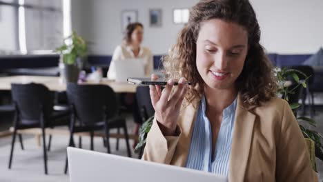 feliz mujer de negocios caucásica hablando en teléfono inteligente y usando portátil en la oficina, cámara lenta
