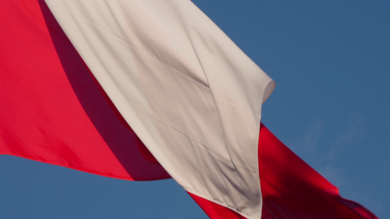 Red and white Polish flag in mid-wave motion, partially blurred by wind, viewed against blue sky. Shot at Warsaw Poland
