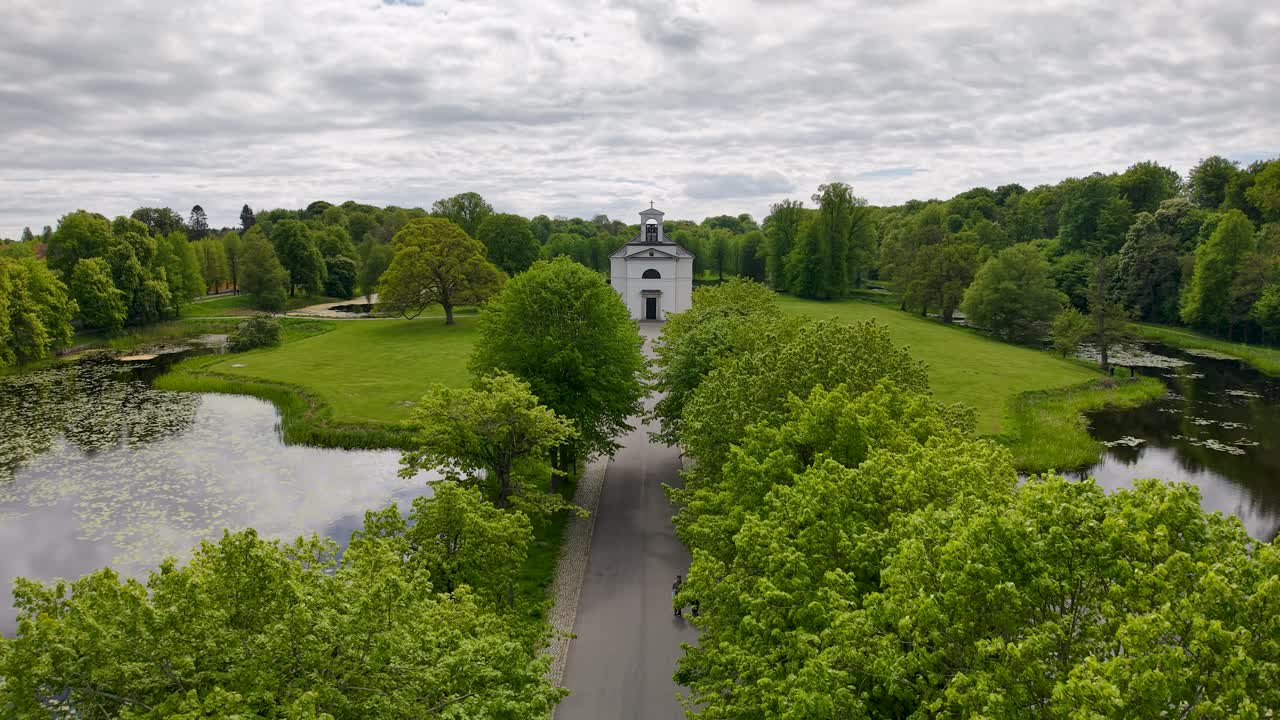 Drone footage showcasing an aerial perspective of a formal garden with symmetrical hedges flanking a waterway and walkway in Denmark