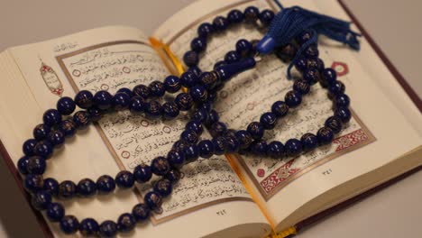 an open quran lying on a table with a prayer beads lying on it, the shot approaches the quran