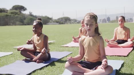 diverse schoolgirls practicing yoga meditation on sunny elementary school playing field, slow motion