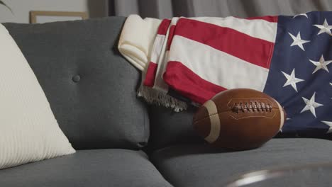 lounge at home of person watching american football game on tv with stars and stripes flag and ball