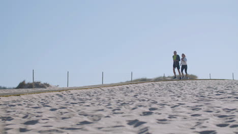 Cheerful-elderly-wife-and-husband-running-along-path-on-seashore