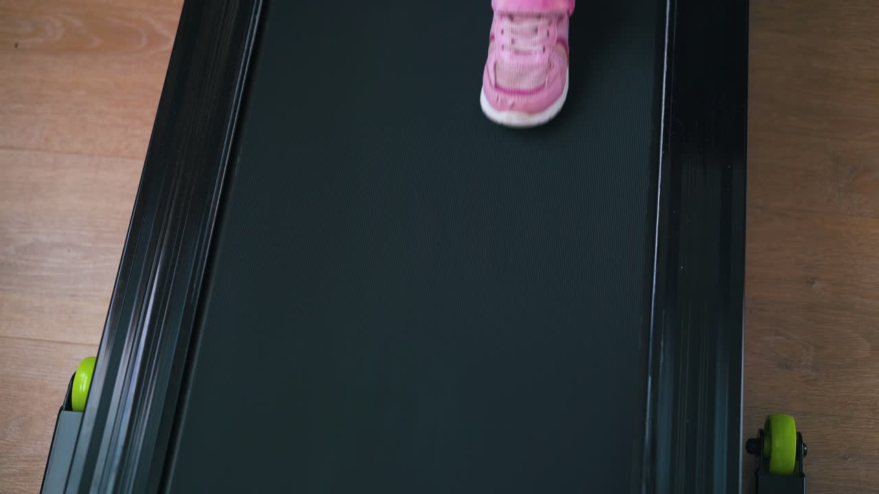 una niña con zapatillas rosadas camina en una cinta de correr en la habitación