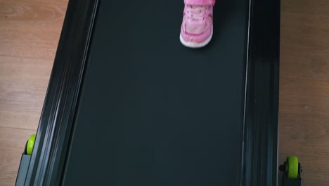 little-girl-in-pink-sneakers-walks-on-treadmill-in-room