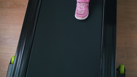 little girl in pink sneakers walks on treadmill in room