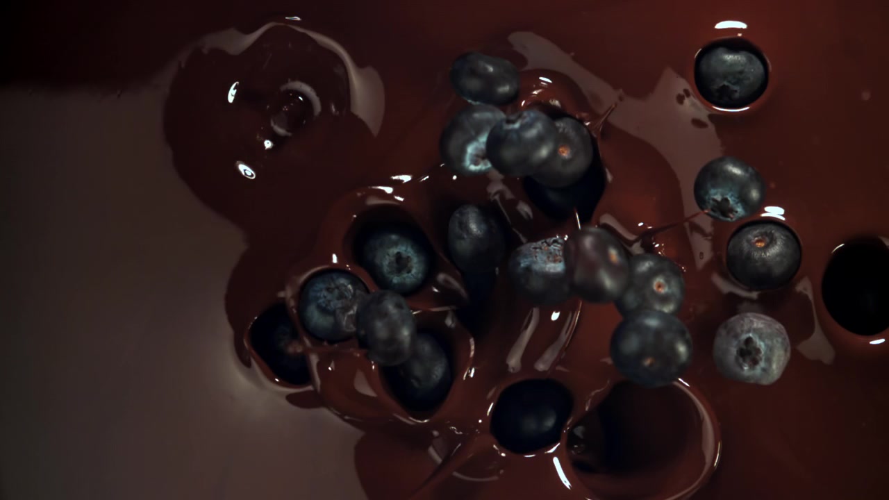 Mirtilli freschi che si tuffano nel cioccolato liquido al rallentatore