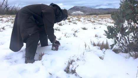 a traditional bushman fills up his billy pot with snow in the australian high country mountains