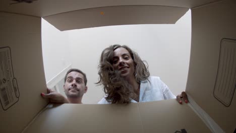 young happy couple opening cardboard box after relocation, looking inside and smiling