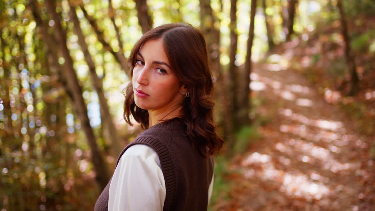 Young woman enjoys autumn walk in sunny forest, feeling relaxed