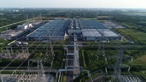 aerial view captures a significant energy facility surrounded by power lines, showcasing the expansive layout of the buildings and equipment under a bright blue sky.