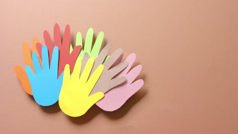 Close-up-of-hands-together-made-of-colourful-paper-on-brown-background-with-copy-space