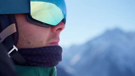 close up of the face of a young man wearing ski goggles while riding the chairlift in snowy mountains