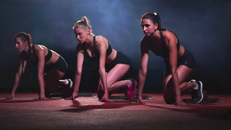 three sports girls in black clothes of the athlete at night on the treadmill will start for the race at the sprint distance from the sitting position.