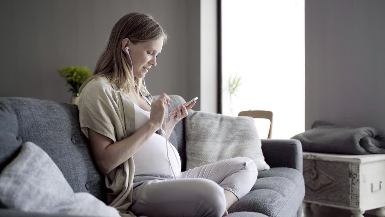 미소 짓는 임산부 가 이어폰 으로 음악 을 듣고 있다