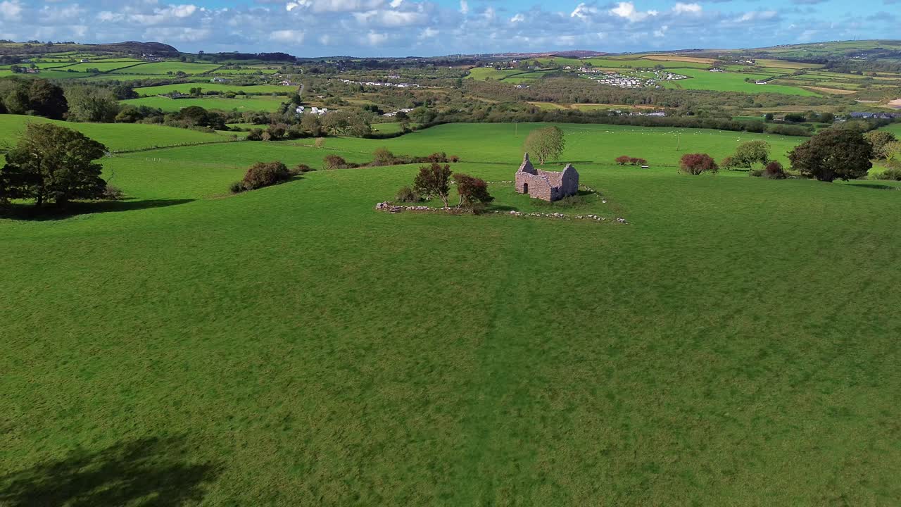 Lligwy chapel aerial view establishing medieval churchyard ruins on lush rolling Welsh meadow field