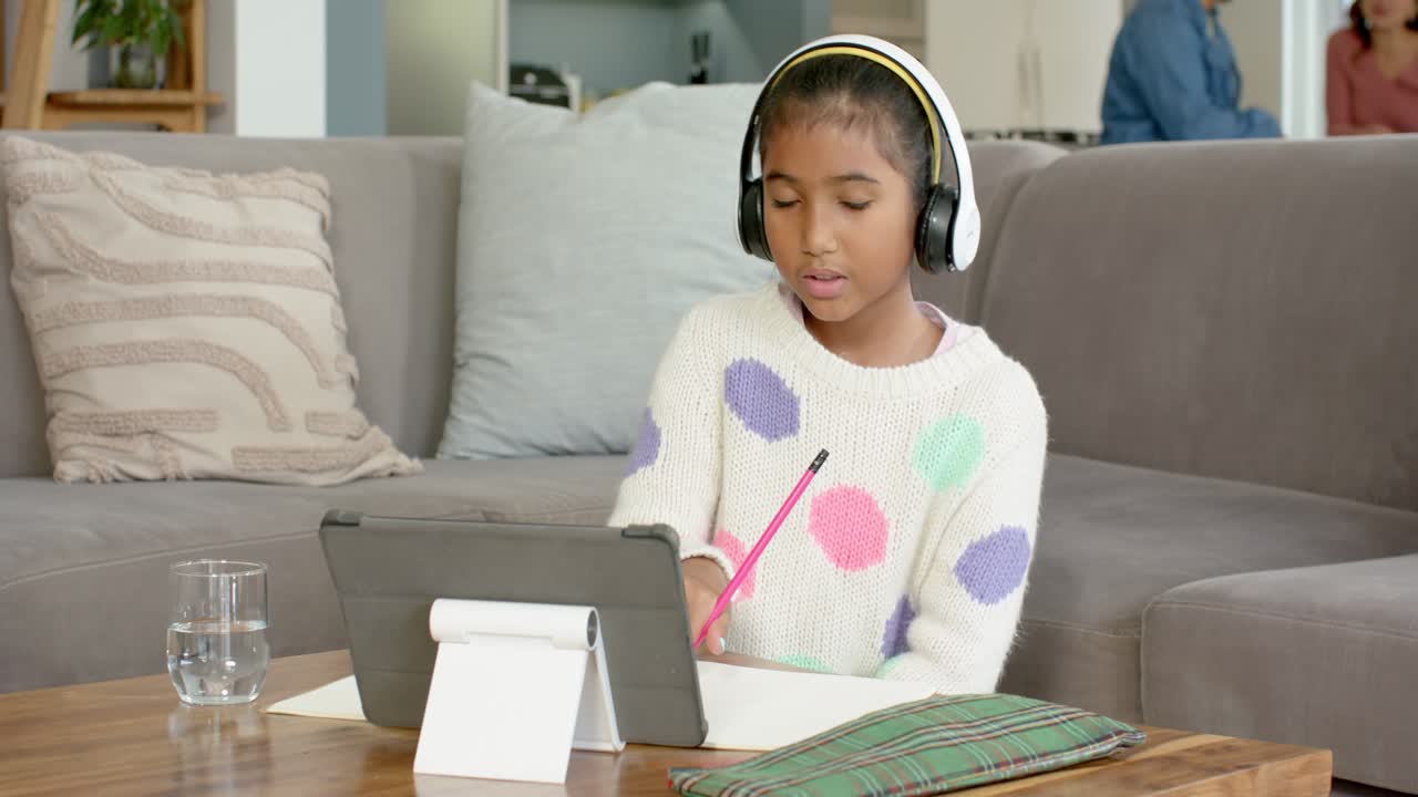 Receiving call, Asian schoolchild launching tablet call jotting notes for homework on sofa